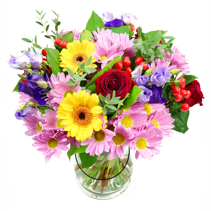 A full, rounded bouquet of mixed seasonal flowers stands proudly in a transparent glass vase, set against a pure white background that throws the shapes and colours into crisp relief. At its heart, sumptuous deep red roses unfold in plush spirals, their velvety texture and rich tone instantly drawing the eye and evoking classic romance. Just alongside, two sunny yellow gerbera daisies with dark brown-orange centres create a lively counterpoint, their wide, daisy-like faces radiating joy and optimism. Around these main blooms, a ring of soft pink daisies and chrysanthemums spreads out, each head composed of many slender petals around tiny yellow eyes, giving the arrangement both softness and generous volume. Threaded through this sea of pink are graceful stems of purple and lavender lisianthus, their elegant, bell-shaped flowers and gentle ruffles adding both height and a cool, sophisticated note that balances the warmth of the reds and yellows. Scattered amidst the petals are small clusters of glossy red hypericum berries, like little beads of colour that lend contemporary texture and a hint of playful energy. A mix of fresh greenery in varied shapes completes the design, from broad, dark leaves that frame the flowers to lighter, more delicate sprigs that add a sense of movement and natural ease. The glass vase reveals straight, neatly cut stems submerged in clear water, a subtle detail that speaks to the care and experience behind the bouquet. This is the sort of arrangement you might see delivered by a Sutton florist to a family home off Banstead Road or an apartment near Sutton station, perfect as a centrepiece for a birthday dinner, a warm housewarming gift, or a thoughtful surprise to brighten someone's everyday routine.